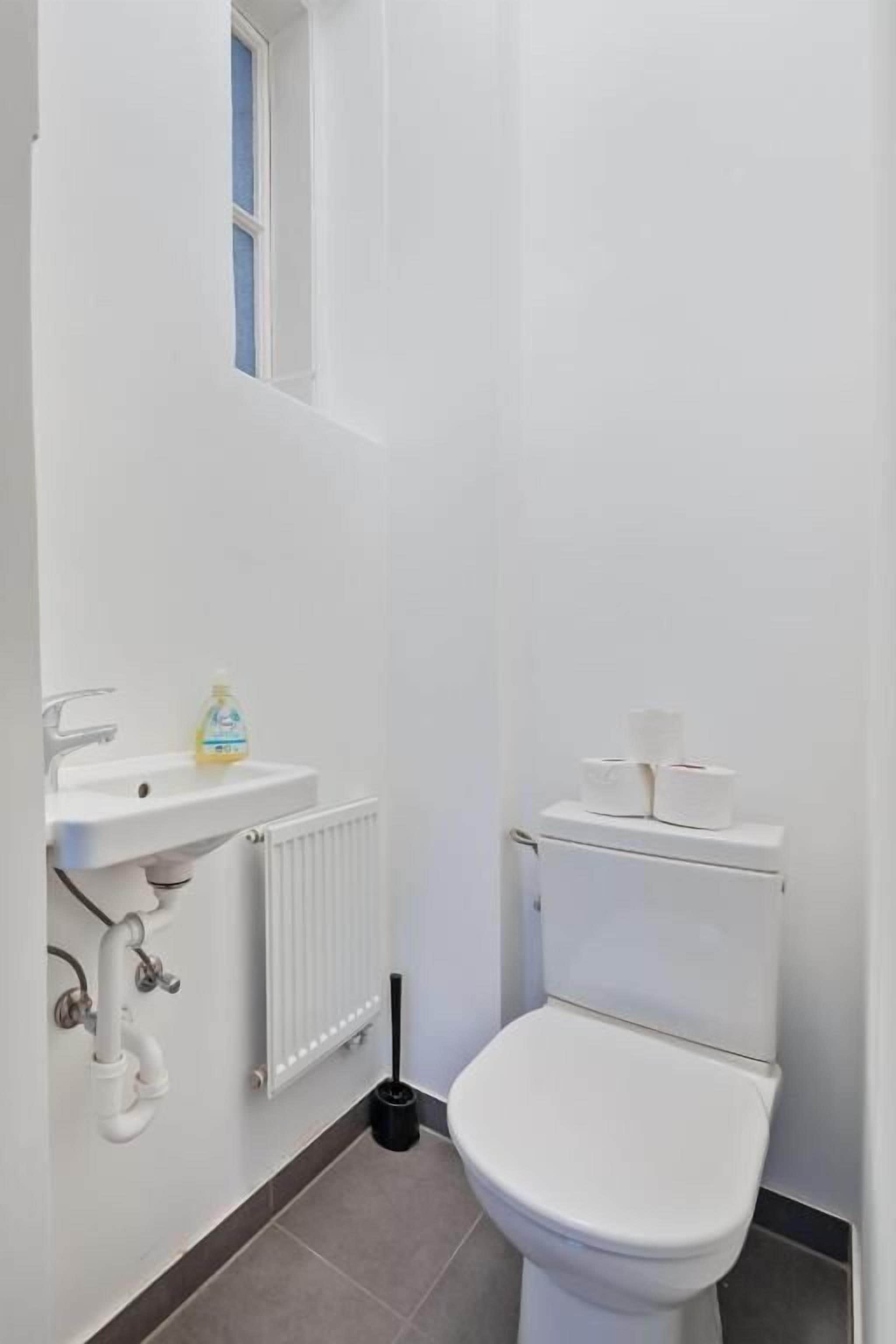 Ein kleines Badezimmer, weiß gehalten, mit Toilette, Waschbecken und Fenster.