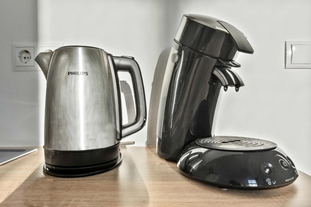 Una tetera de acero inoxidable y una cafetera negra sobre una encimera de madera.