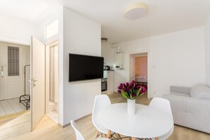 A modern living room with a flat-screen TV, a dining table with chairs, and a sofa. - Cityswap- Wien Naschmarkt (Wien)