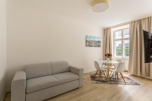 Una sala de estar con sofá, una mesa de comedor con sillas, televisor y ventana con cortinas.
