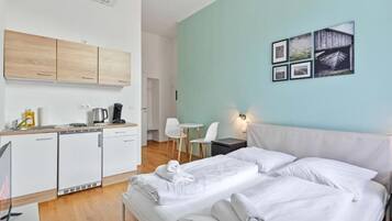 A hotel room with a bed, a small table, a chair, a kitchenette, and a wall with pictures.