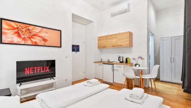 A modern hotel room with a flat-screen TV displaying 'NETFLIX,' a bed, a small kitchenette, and a dining area. - Cityswap- Wien Naschmarkt (Wien)