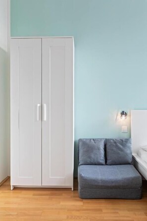 Una habitación con un armario blanco, un sofá gris y una lámpara fijada a la pared.