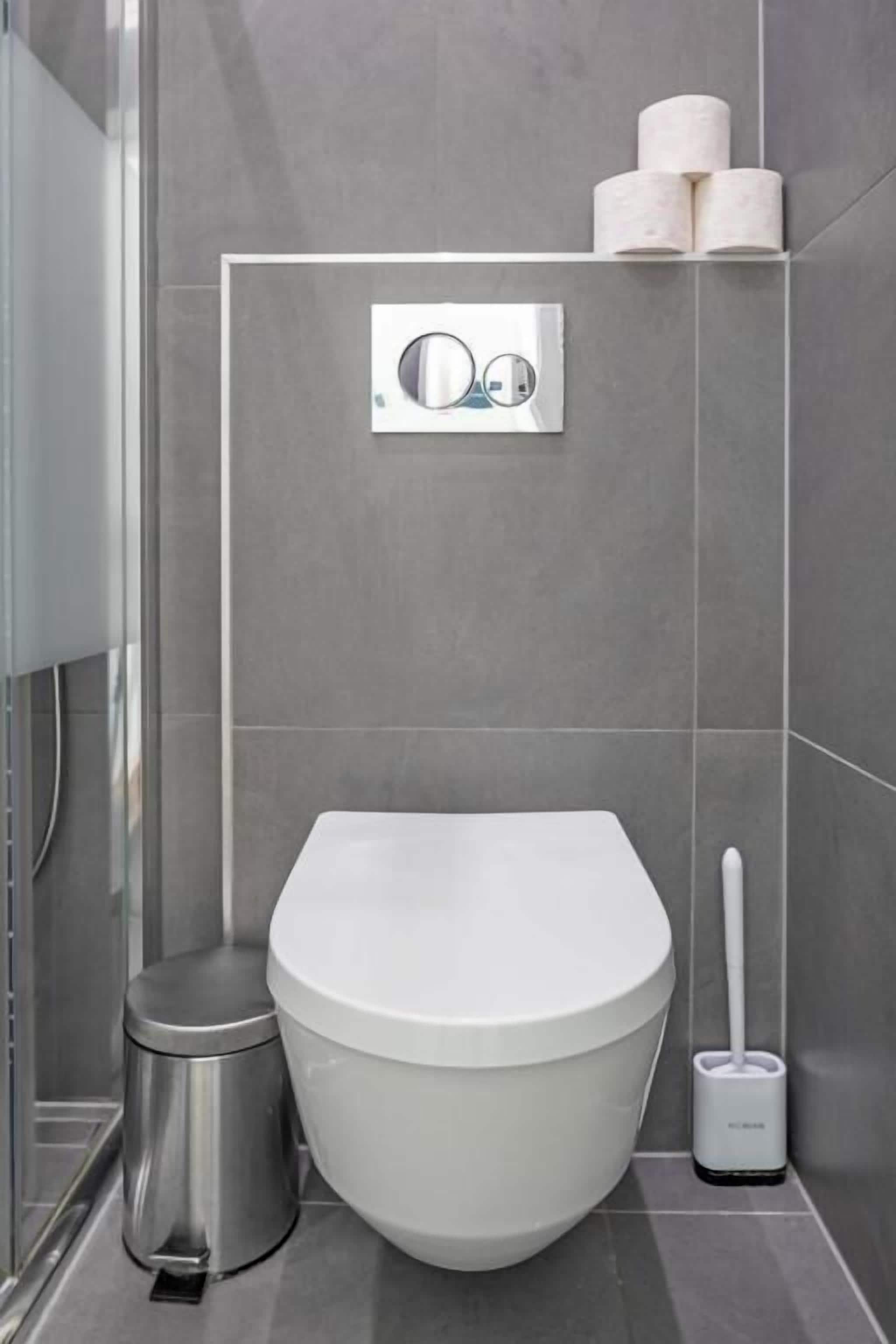 A modern bathroom with a toilet, bidet, and toilet paper dispenser.
