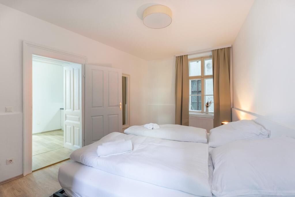 Et hotelværelse med to senge, et vindue med gardiner, en dør der fører til et andet værelse og en loftlampe.