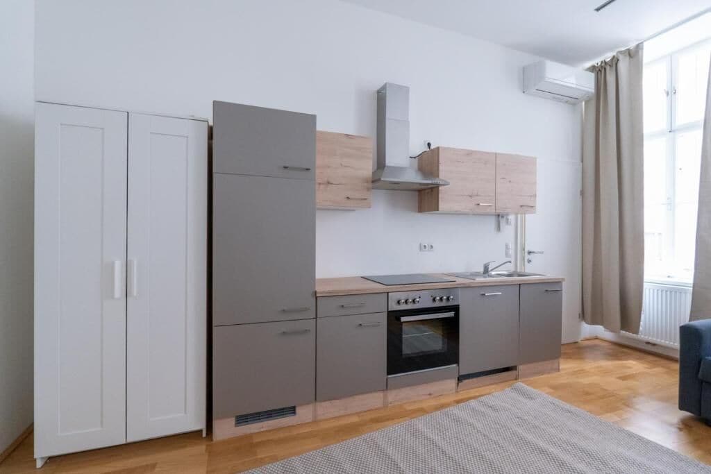 Eine moderne Küche mit grauen Schränken, einem eingebauten Backofen und einem Fenster mit Vorhängen.