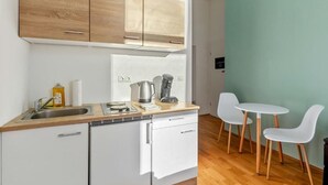 A compact kitchen with a sink, a kettle, and a coffee maker. There are two white chairs and a small table. - Cityswap- Wien Naschmarkt (Wien)