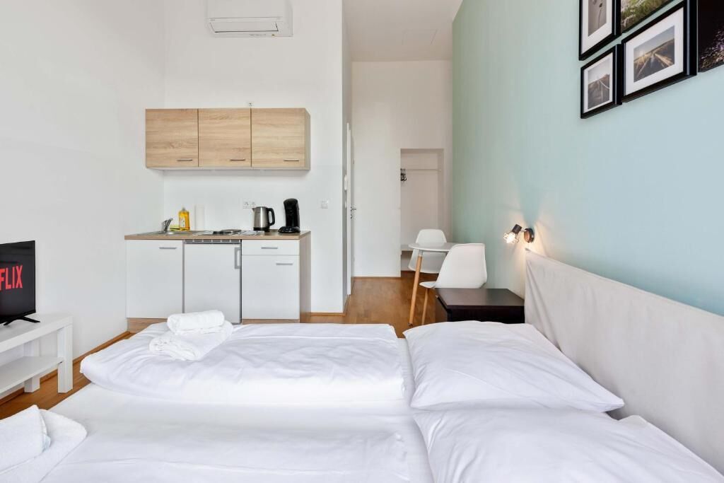 A hotel room with a bed, a desk, a kitchenette, and a TV.