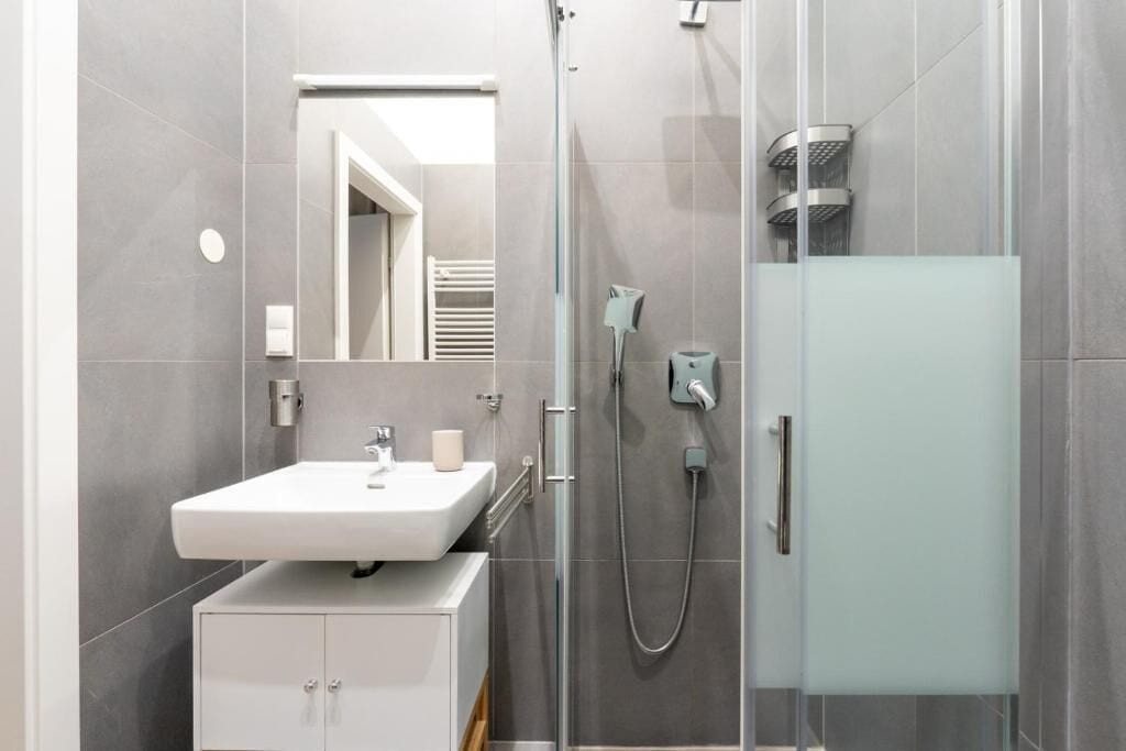 Ein modernes Badezimmer mit einem weißen Waschbecken, einer Duschkabine aus Glas und einem Schrank.