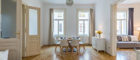 A dining area with a table set for two, a sofa, and a lamp.