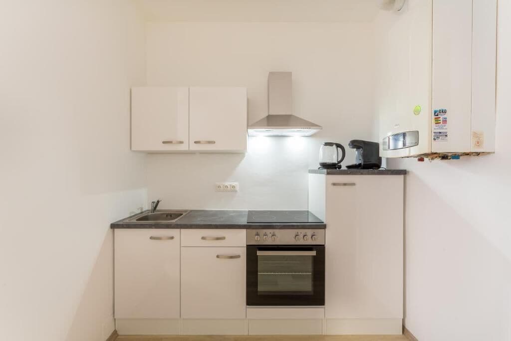Una cocina compacta con gabinetes blancos, estufa, microondas y tetera.