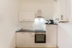 A compact kitchen with white cabinets, a stove, a microwave, and a kettle. - Cityswap- Wien Naschmarkt (Wien)
