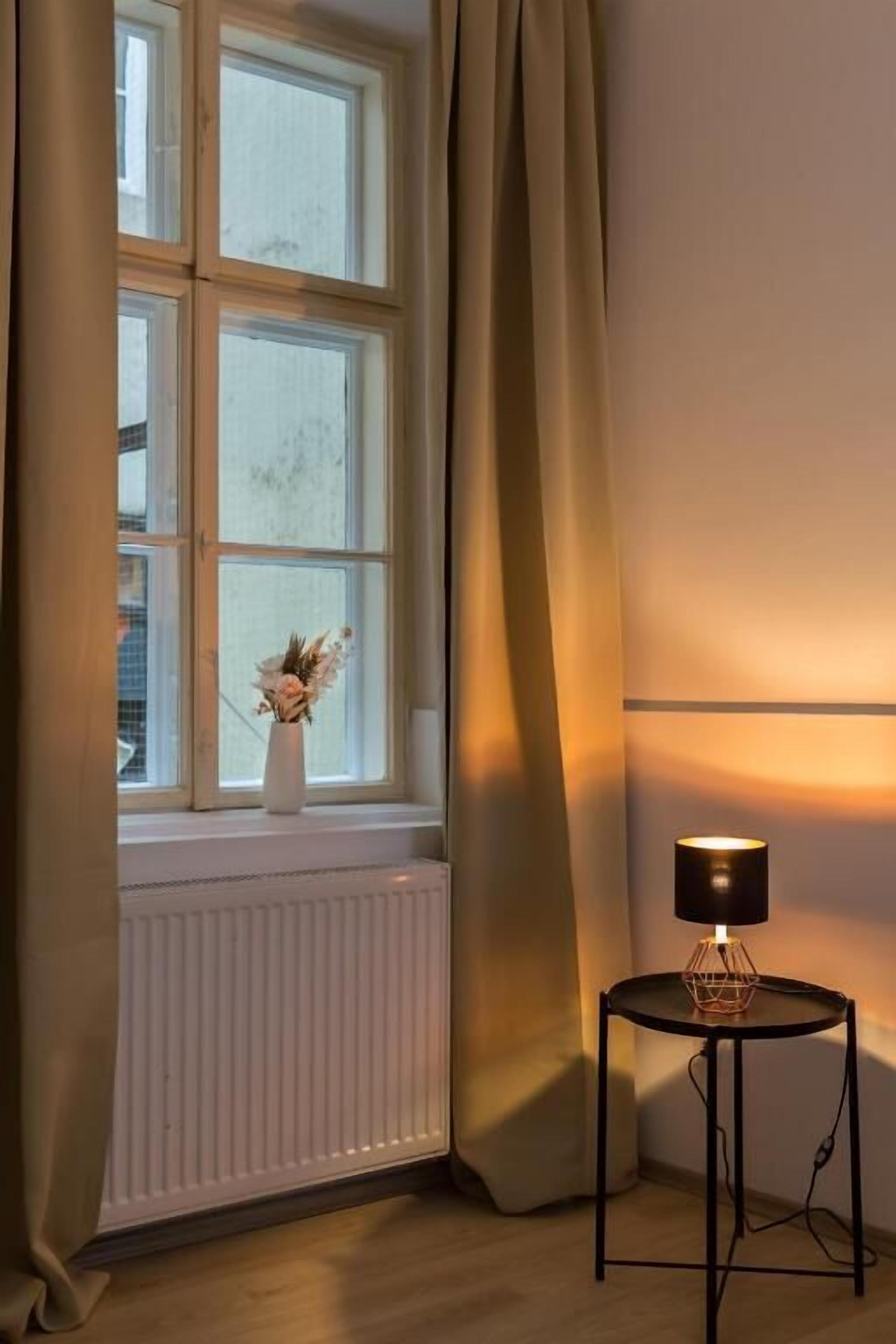 Et værelse med en radiator, et bord med lampe og et vindue med gardiner.