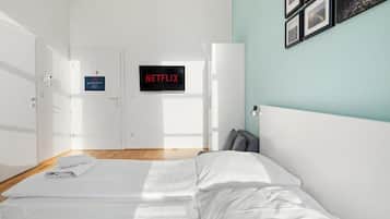 Hotellihuone, jossa on sänky, ovi, jossa on kyltti, seinälle asennettu televisio ja kehystetyt valokuvat.