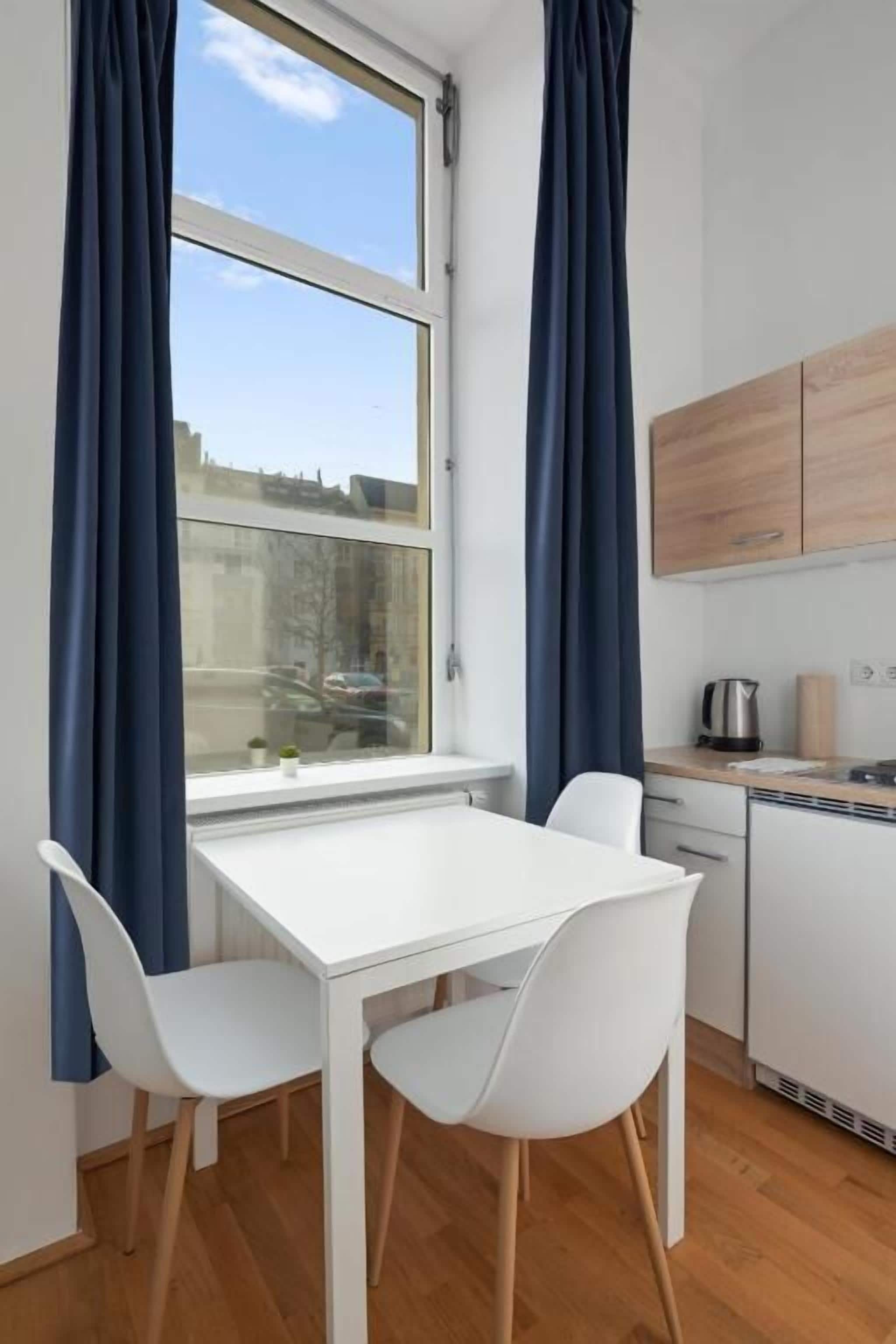Een gezellige, kleine keuken met een witte tafel en stoelen, een raam met gordijnen en uitzicht op het omliggende landschap.