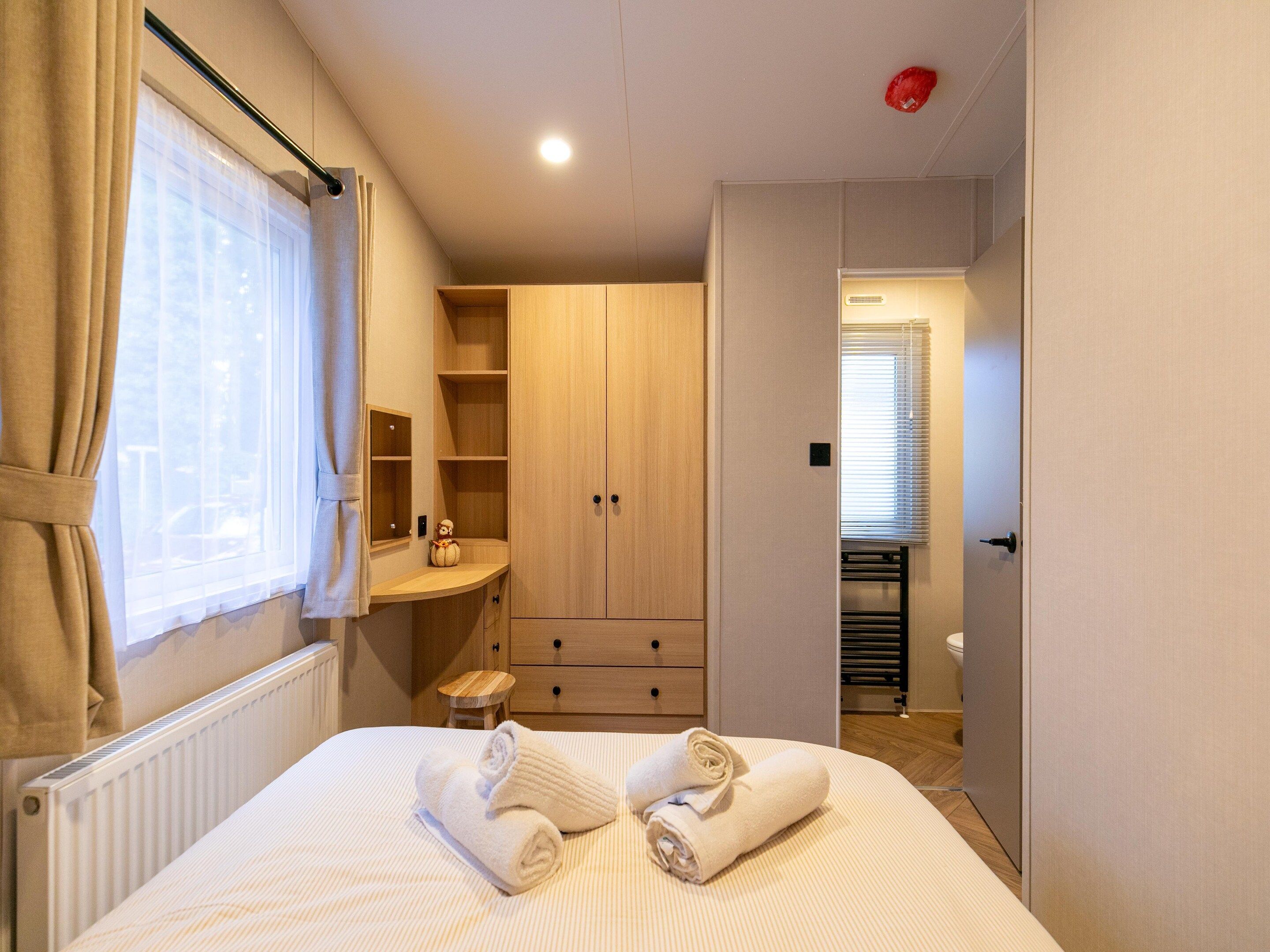 A hotel room with a bed, a wooden wardrobe, a small wooden stool, and a radiator.