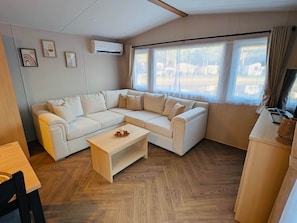 A modern living room with a sectional sofa, a wooden coffee table, and a large window with curtains.