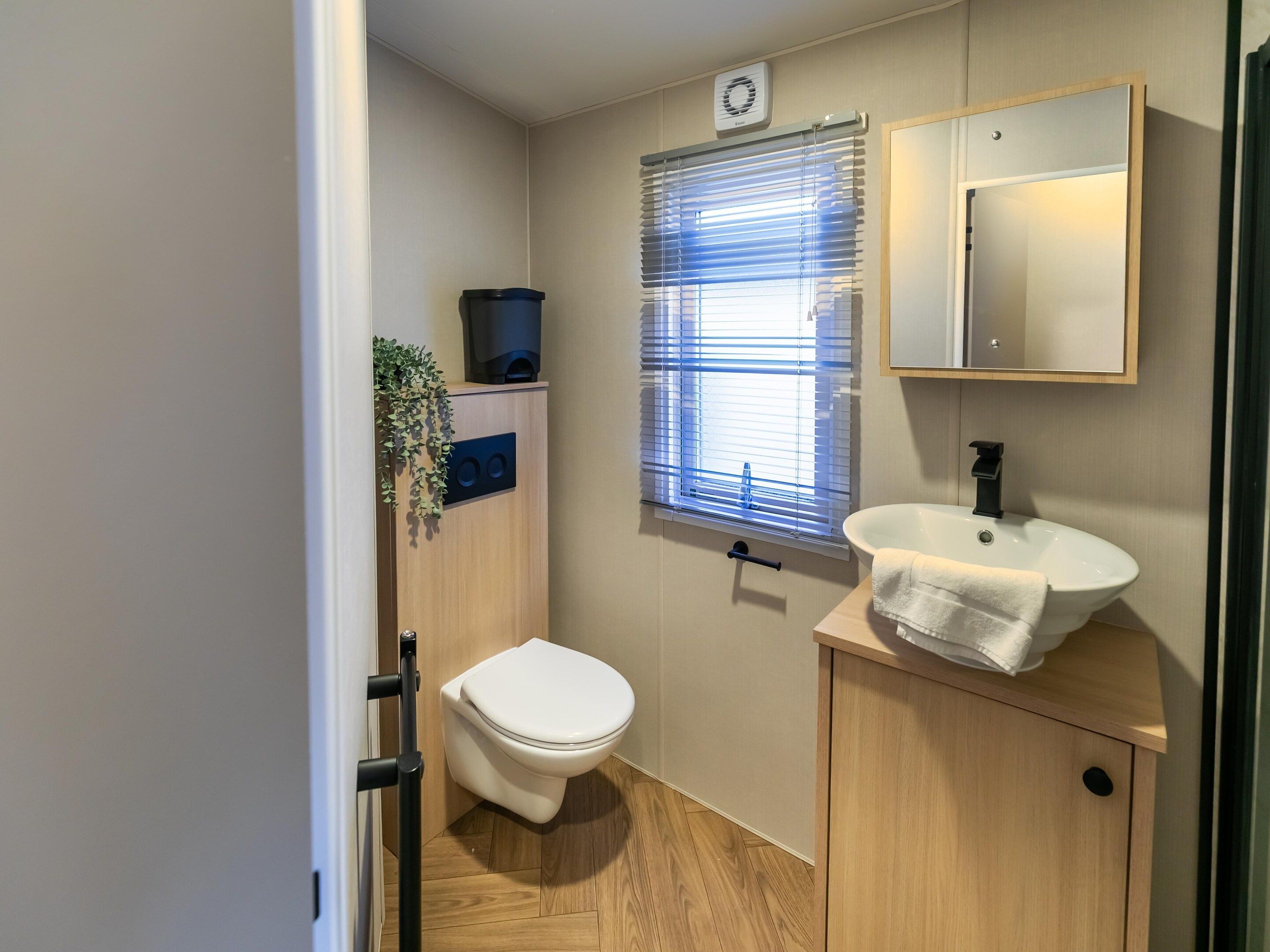 A compact bathroom with a toilet, sink, and window with blinds.