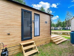 Una cabaña de madera con puerta y ventana, un pequeño escalón de madera y un cilindro de gas.
