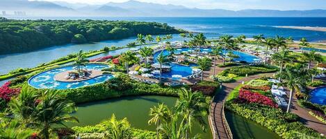 A resort with multiple swimming pools, a boardwalk, and lush greenery.