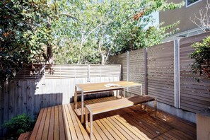 Eine Holzterrasse mit Tisch und Bänken, umgeben von einem Holzzaun und Bäumen.