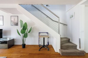 Ein modernes Wohnzimmer mit Treppe, Holzboden, einer Topfpflanze und einem Schreibtisch mit Computer.