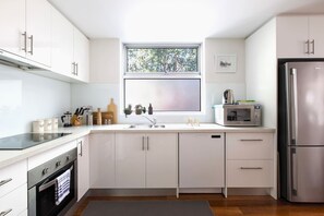 Eine moderne Küche mit weißen Schränken, einem Edelstahlkühlschrank, einer Mikrowelle und einem Fenster mit Blick auf Bäume.