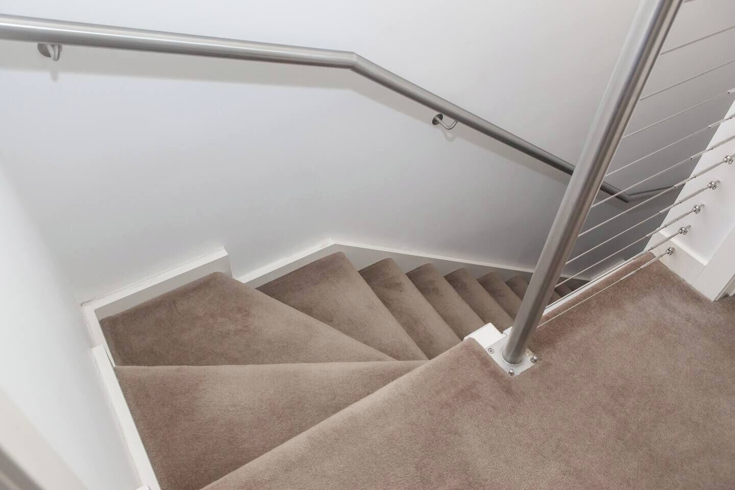 A carpeted staircase with a metal handrail and a white wall.