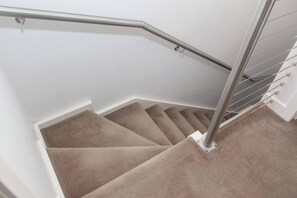 Un escalier recouvert de moquette, doté d’une rampe métallique et bordé d’un mur blanc.