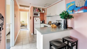 A modern kitchen with a central island, a microwave, and a refrigerator. There is a dining area visible in the background. - Coral Atelier Bright Artistic Hideaway in the CBD (Melbourne)