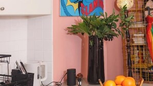 A kitchen with a washing machine, a vase with plants, a fruit bowl, and a colorful painting on the wall. - Coral Atelier Bright Artistic Hideaway in the CBD (Melbourne)