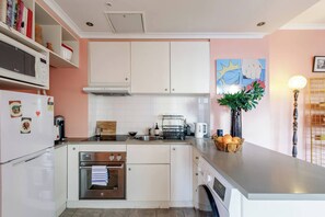 Une cuisine de taille réduite, avec des meubles blancs, un four à micro-ondes, une machine à café et un évier.