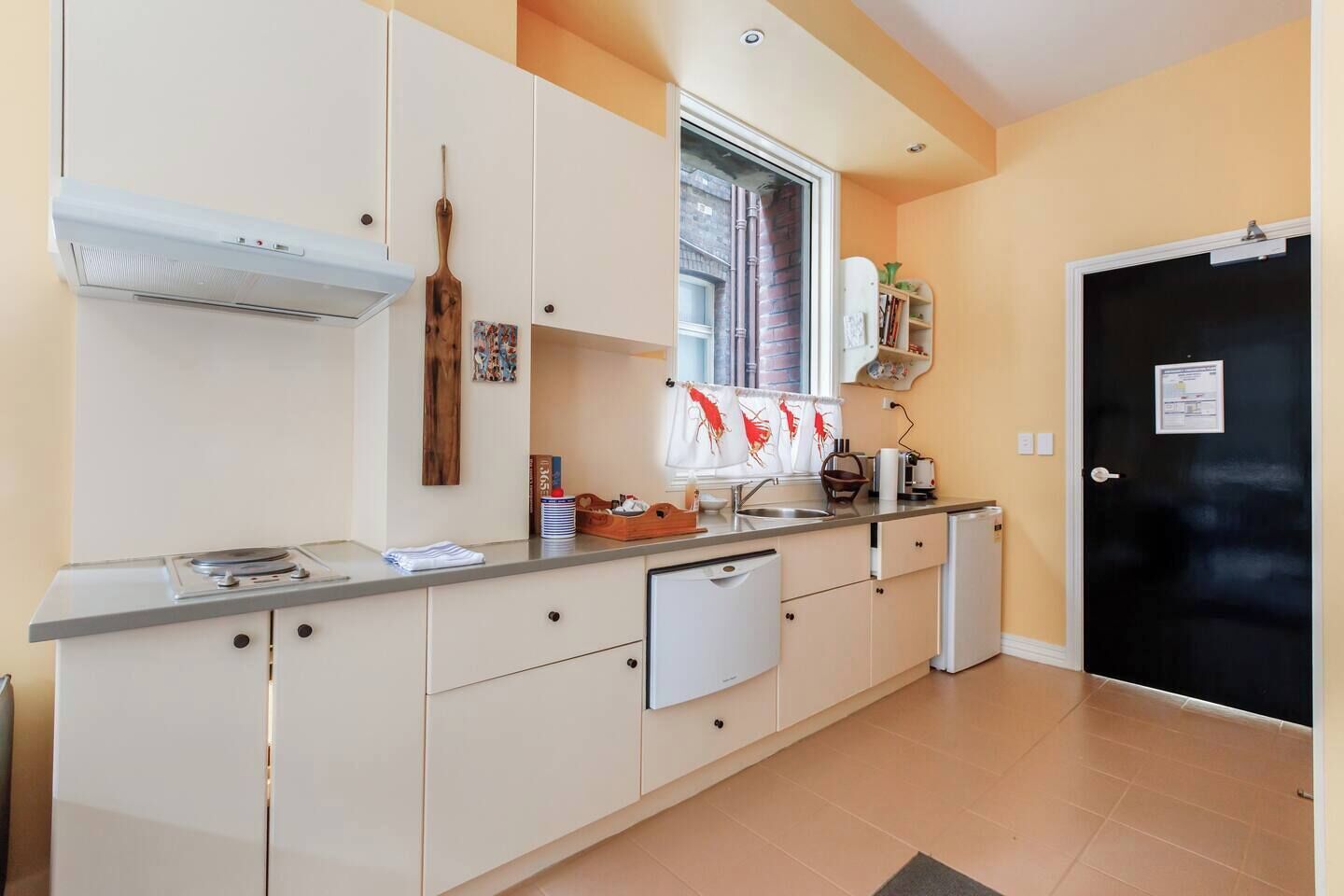 Une cuisine compacte équipée d’une cuisinière intégrée, d’un petit réfrigérateur et d’une fenêtre avec des rideaux.