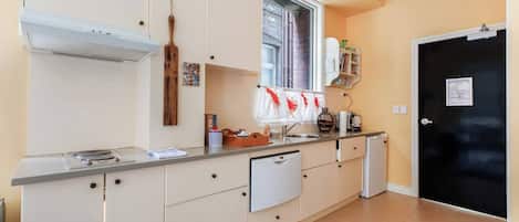A compact kitchen with a built-in stove, a small refrigerator, and a window with curtains.