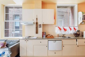 Eine moderne Küche mit weißen Schränken, einem eingebauten Geschirrspüler und einem Fenster mit Blick auf ein Backsteingebäude.