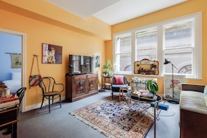 A living room with a large window, a television, a bookshelf, and a patterned rug. - Romantic Bohemian Hideaway in the Melbourne CBD (Melbourne)