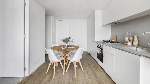 Una cocina moderna con armarios blancos, una mesa de comedor de madera y dos sillas blancas.
