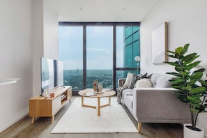 Ein modernes Wohnzimmer mit großem Fenster, einer Couch, einem Couchtisch und einem Fernseher.