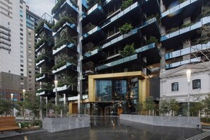 A modern multi-story building with balconies, a central entrance, and surrounding greenery. - A Sky high Metropolis Retreat near the CBD (Southbank)