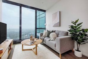 Ein modernes Wohnzimmer mit großem Fenster, einem grauen Sofa, einem runden Couchtisch und einer Topfpflanze.
