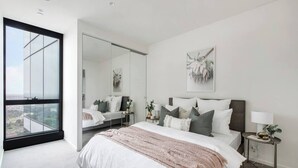 Un dormitorio moderno con una cama grande, una mesita de noche, un espejo y vistas amplias por una ventana grande.