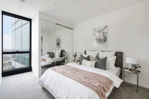 Ein modernes Schlafzimmer mit einem großen Bett, einem Nachttisch, einem Spiegel und Blick durch ein großes Fenster.