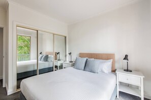Ein Hotelzimmer mit einem großen Bett, einem Nachttisch, einem Schreibtisch und einem Schrank mit Spiegel.