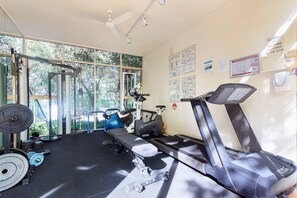 Ein Fitnessraum mit Trainingsgeräten, Laufband und einer Gewichtshalterung.