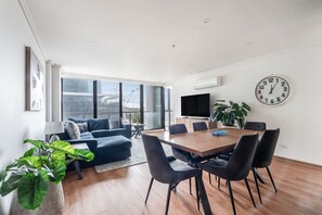 A modern living space with a dining area, a large window, and a wall-mounted clock. - Sentinel Vista Urban Stay with Pool and Tennis Court (Southbank)