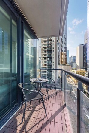 A balcony with a glass railing, a table, and two chairs. - Sentinel Vista Urban Stay with Pool and Tennis Court (Southbank)