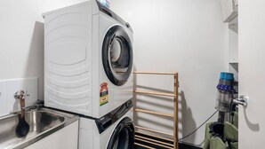 Ett kompakt tvättrum med en tvättmaskin och en torktumlare som båda har frontmatning, en diskho i metall och en torkställning.