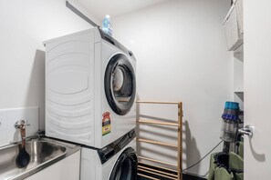A compact laundry area with a front-loading washer and dryer, a metal sink, and a drying rack. - Sentinel Vista Urban Stay with Pool and Tennis Court (Southbank)