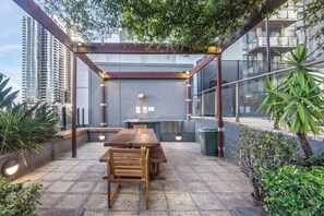 An outdoor patio with a wooden table and chairs, a grill, and potted plants. - Sentinel Vista Urban Stay with Pool and Tennis Court (Southbank)