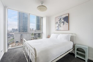 A bedroom with a large window, a bed, a bedside table, and a painting on the wall. - Sentinel Vista Urban Stay with Pool and Tennis Court (Southbank)